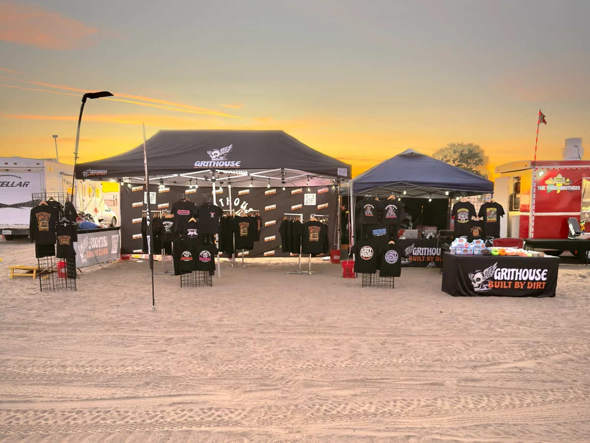 Grithouse's two-canopy booth at sunset, with branded tent, shirt displays, and front table.